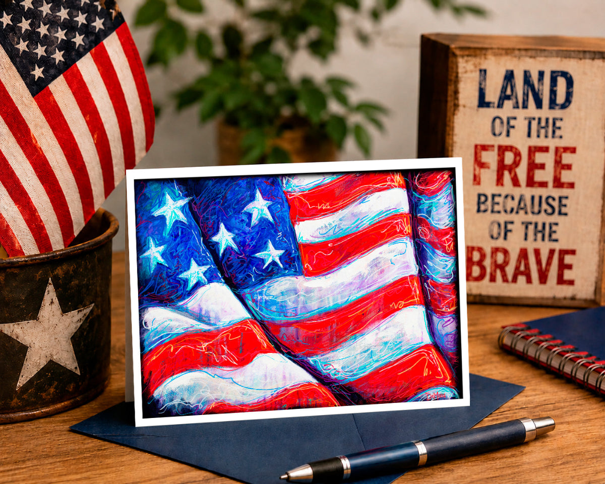 Colorful American flag painting on a wooden table with an American flag, plant, and 'Land of the Free Because of the Brave' sign in the background.